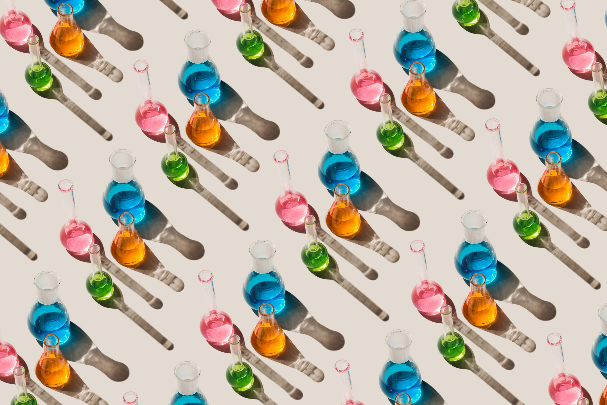 Pattern of laboratory glassware with multicolored liquids on beige background. Natural medicine, cosmetic research, bioscience, organic skin care products. Top view, flat lay.