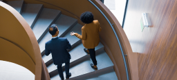 Photo of two business colleagues in conversation while walking up a modern, curved staircase. (credit: Getty Images)