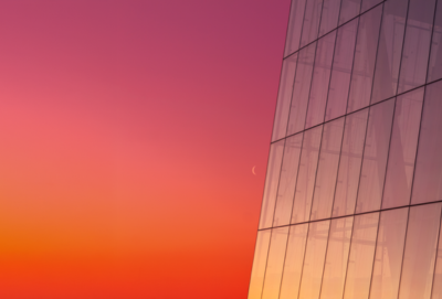 Off-center, zoomed-in capture of a glass skyscraper amid pink-orange sunset backdrop (Source: Getty Images)